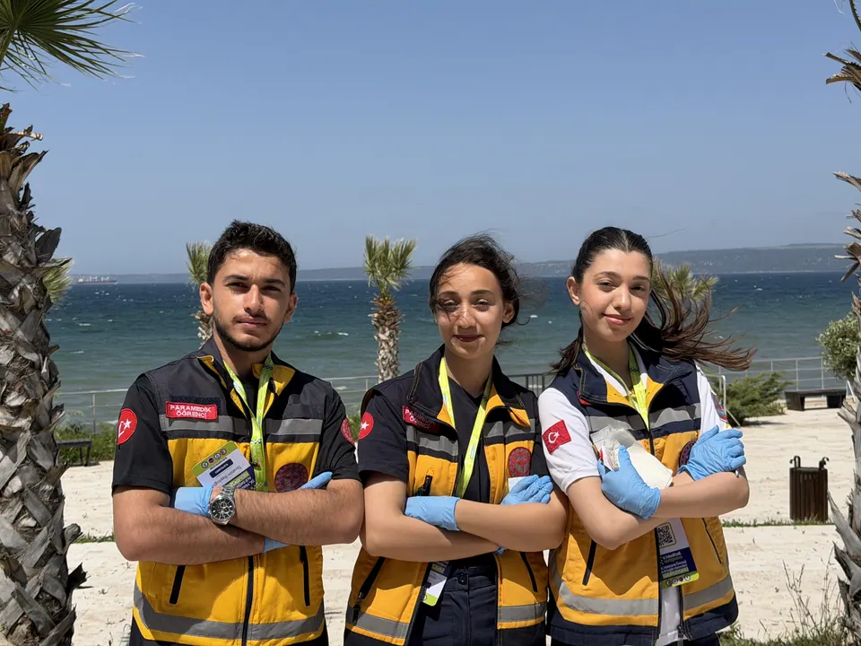 Sarı yelekli üç yarışmacı deniz önünde